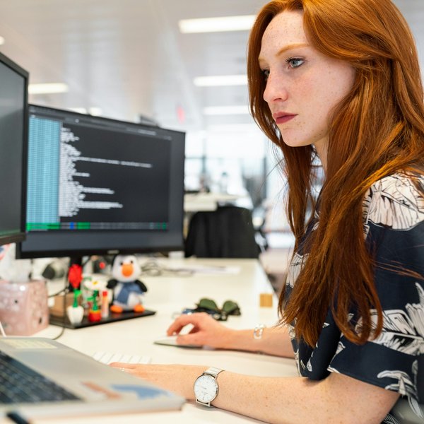 Entwicklerin arbeitet konzentriert an zwei Bildschirmen mit Code